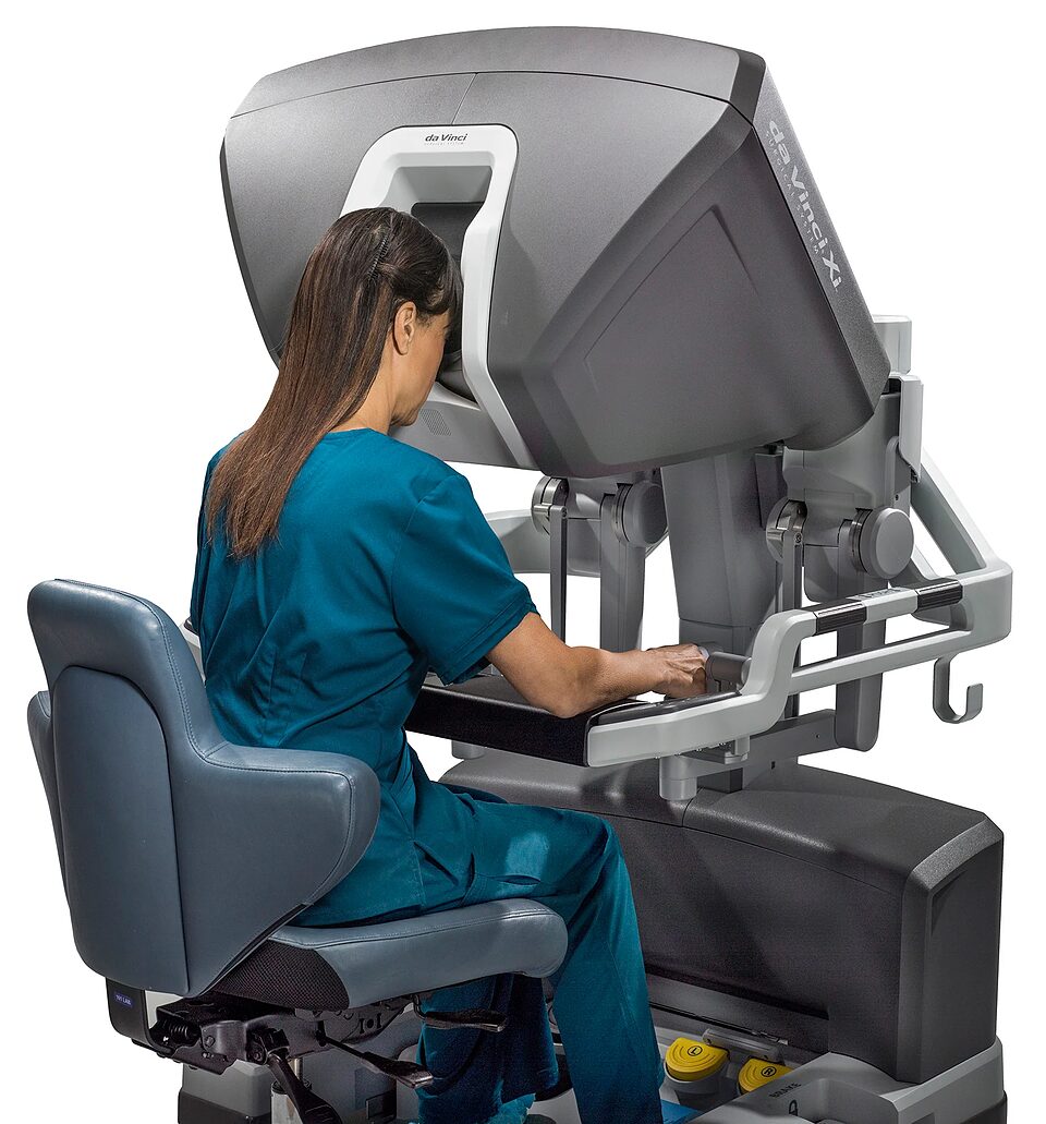 Surgeon seated at a closed robotic surgery console, looking into its stereo viewer